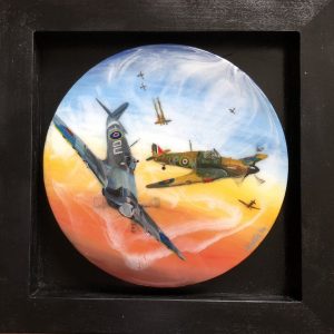 Black frame with a circle art piece in resin and acrylic depicting a sunset sky and planes dog fighting in the foreground